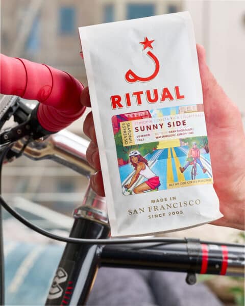 Hand holding a bag of espresso on top of bike handle bar.