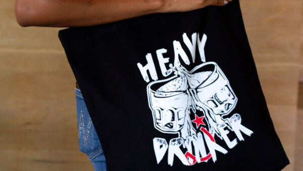 Person wearing black tote bag that says "heavy drinker"